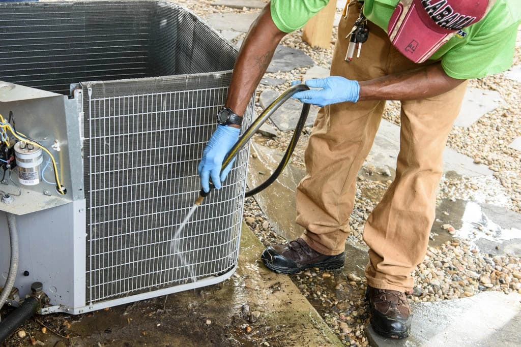 A Myers Comfort Specialists technician cleaning an outdoor unit on a service call
